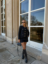 a lady wears a black tweed cropped jacket with matching shorts